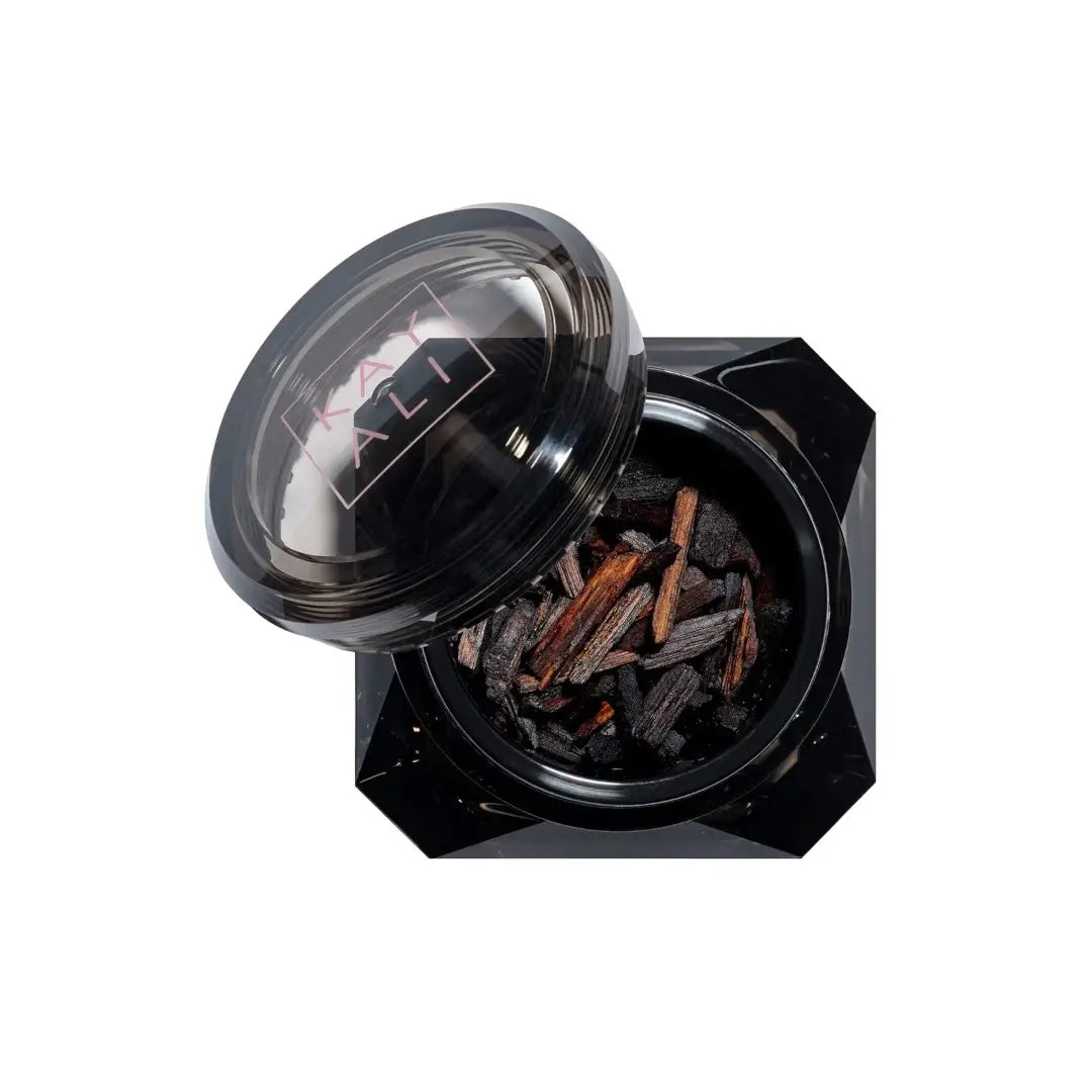 Black container with lid open, revealing 'Oudgasm Rose Oud Perfumed Oud Wood' on a white background with 'Kayali' branding
